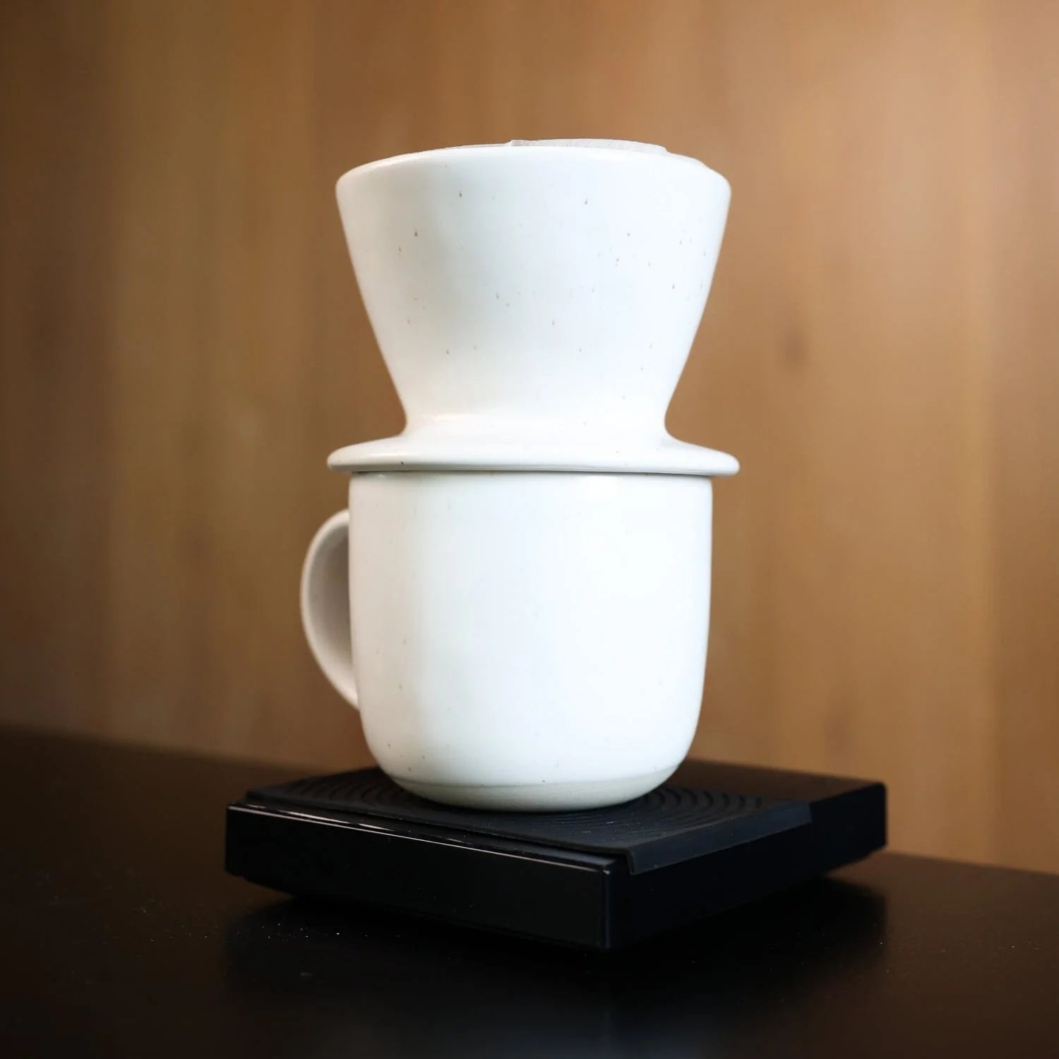 White ceramic coffee maker with a cup on a wooden surface