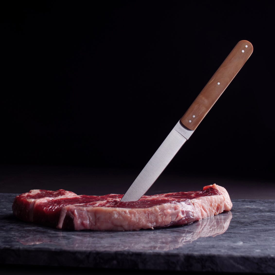 Fable steak knife with raw steak on dark surface